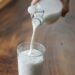 crop person pouring milk into glass on table