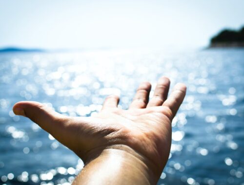 person hand reaching body of water